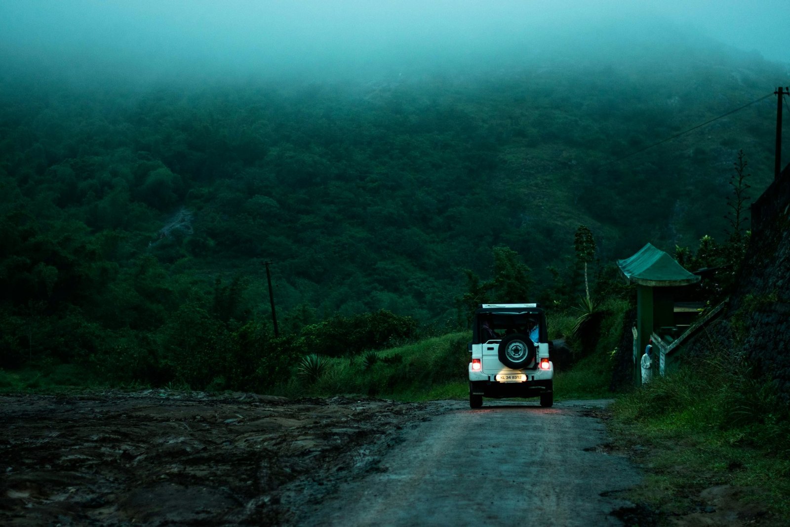 A blue SUV driving along a misty forest road in the hills